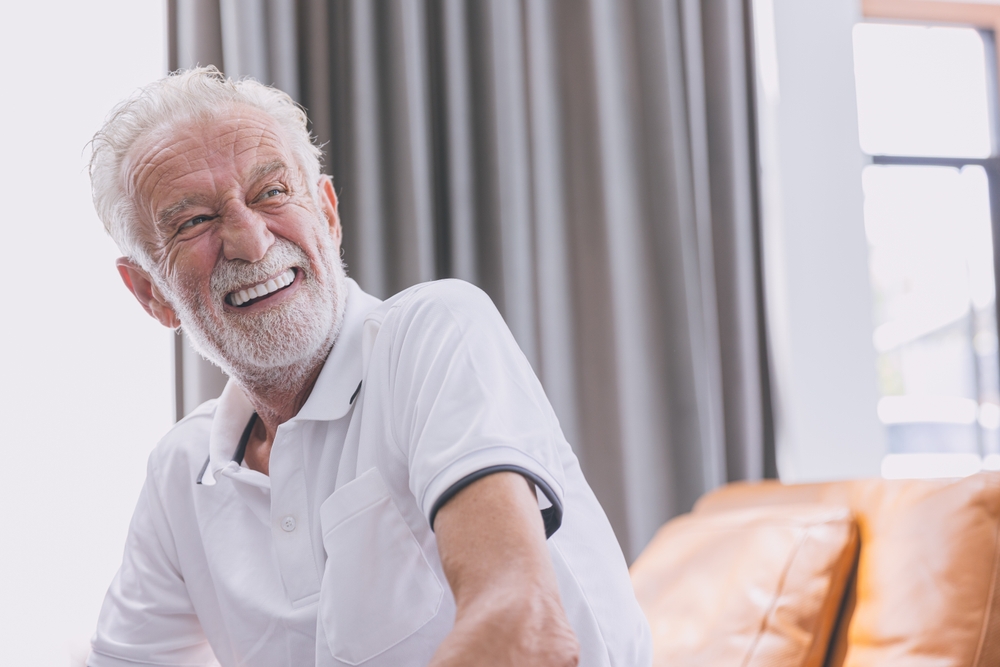 Smiling elderly man in a white shirt, showcasing confidence and happiness, reflecting the positive impact of dental implants on quality of life.