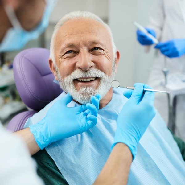 Smiling elderly man in dental chair receiving examination from dentist in blue gloves, showcasing dental care and oral health.