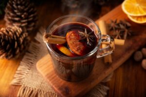 Mulled wine in a glass mug, garnished with orange slices, cinnamon sticks, and star anise, on a wooden surface with pinecones, representing festive holiday beverages and their impact on dental health.